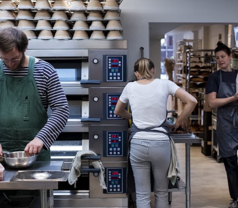 Two women and a man wearing aprons working in an artisan bakery.